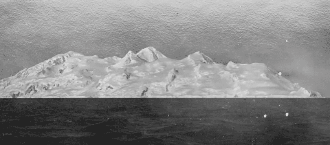 An old image of Antarctica, with a snowy landscape and mountains in the background.