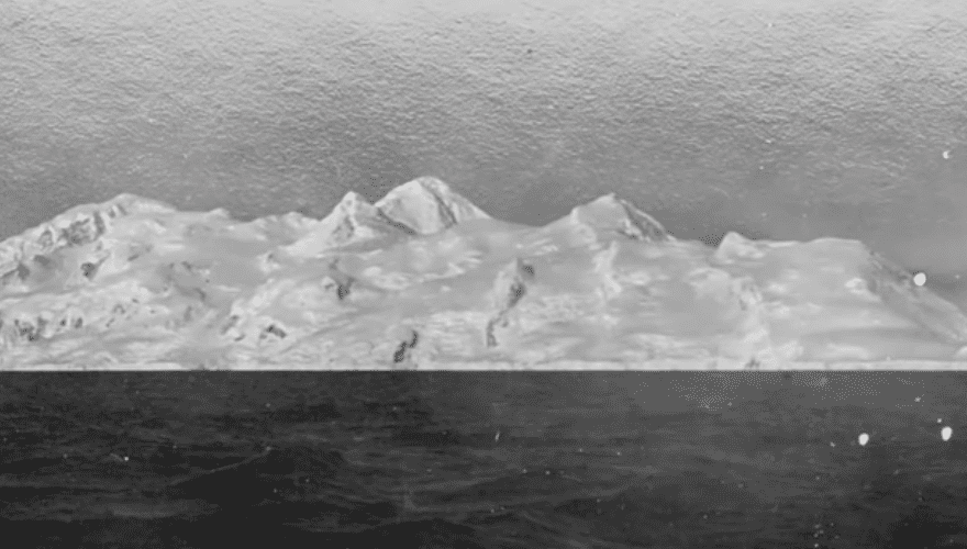 An old image of Antarctica, with a snowy landscape and mountains in the background.