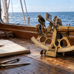 Brass marine sextant on a chart table aboard a sailboat with the sea horizon beyond