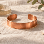 Conceptual illustration of a generic open copper cuff beside a measuring tape and blank notebook.